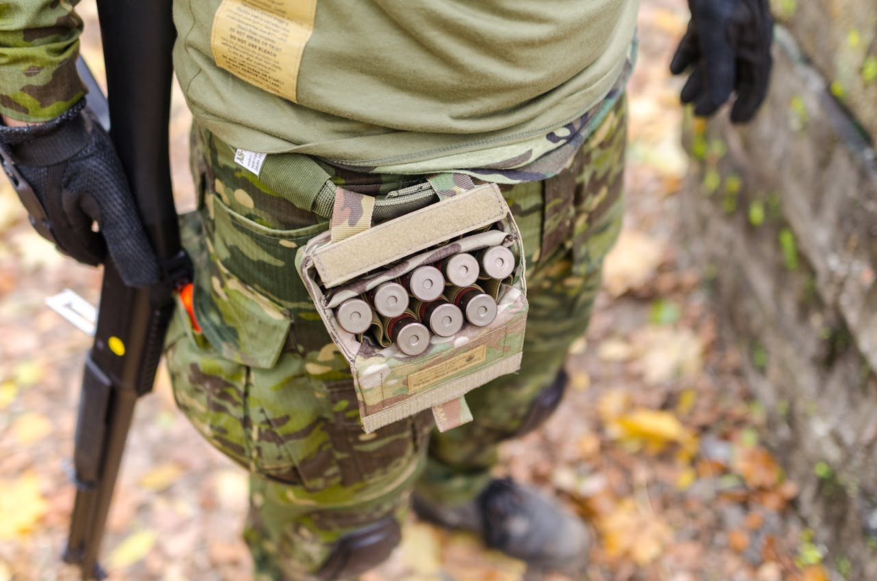 about-us Close-up of a soldier in camouflage uniform with ammunition and shotgun outdoors.