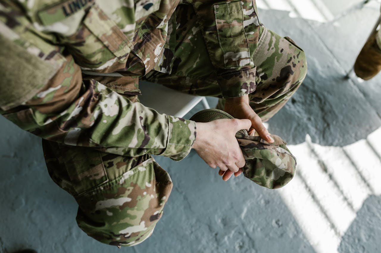 Soldier adjusting combat boots, focused on military uniform in daylight.